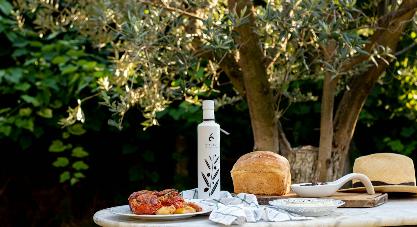 Bottiglia di olio d'oliva Etolea con pane e pomodori ripieni all'aperto.
